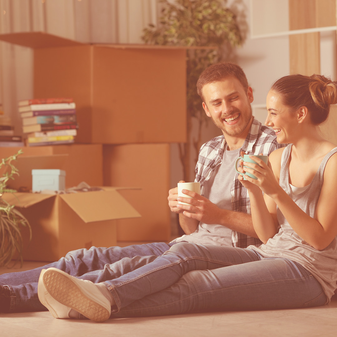 couple sitting on floor with moving boxes drinking coffee
