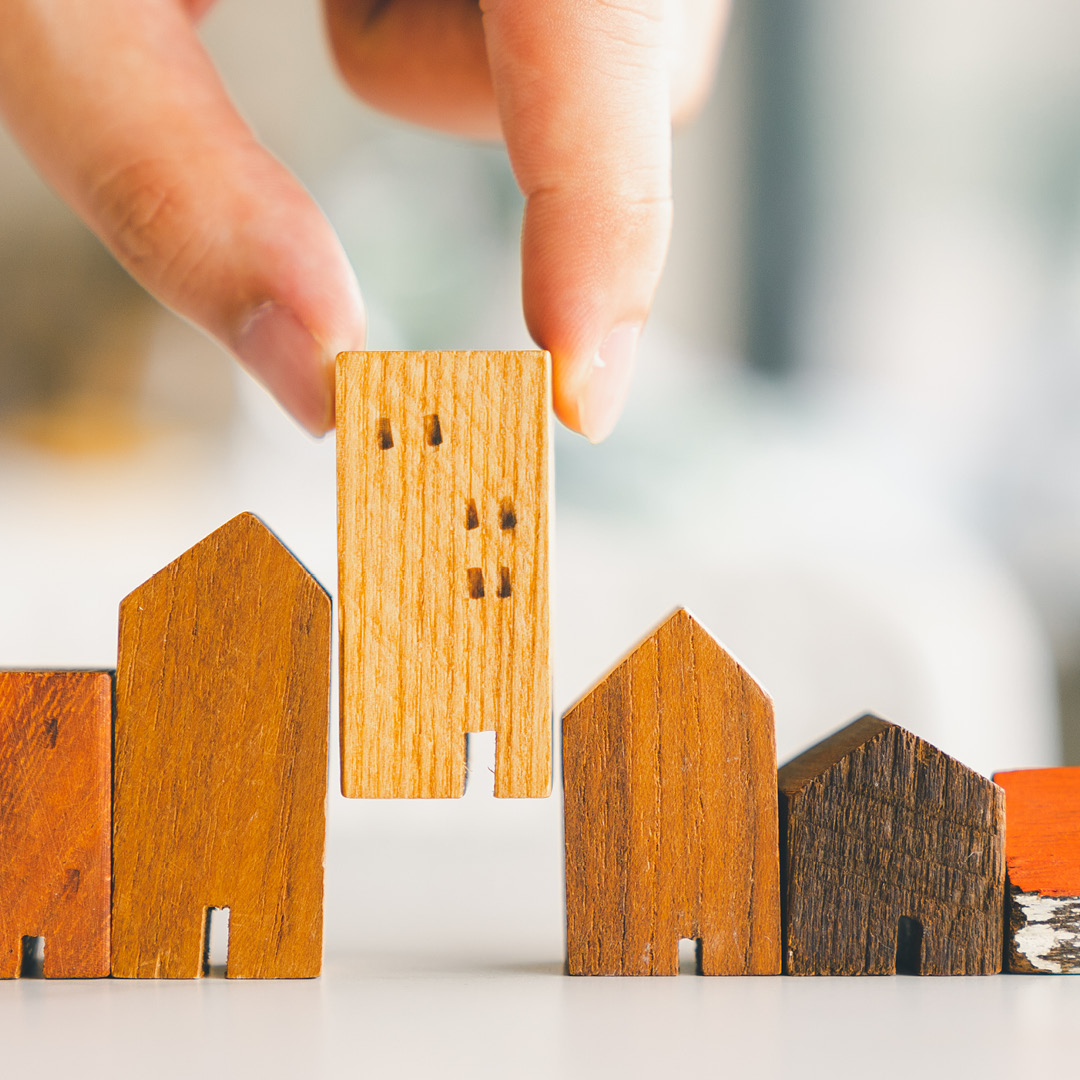 Hand placing small block house model with line of other house models